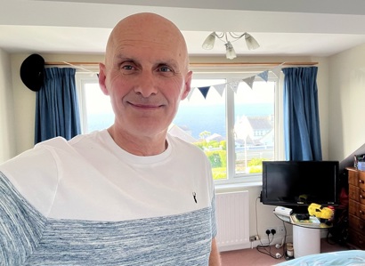 A photo of Christie prostate patient Andy Fleet in a a bedroom with a window and bunting behind him.