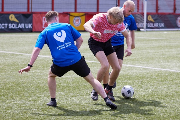 A photo of 3 people playing football, 2 people wearing Christie Charity t-shirts.