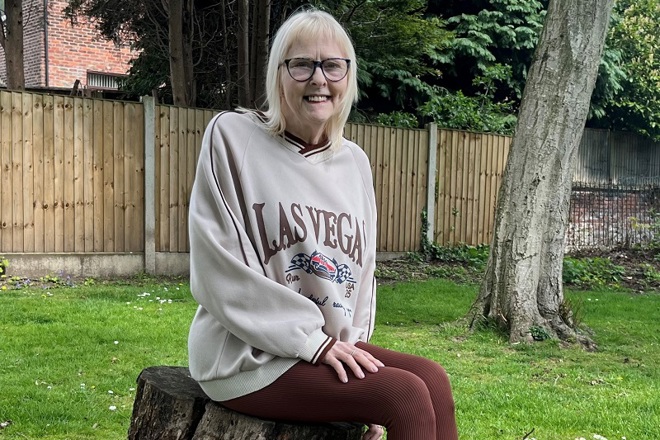 A photo of Christie patient Jan Smith sitting on a tree stump.