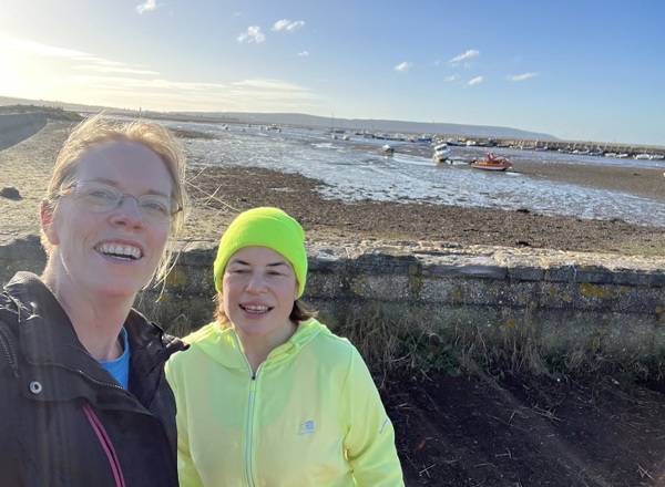A photo of Claire White and Chantal Neal standing at the coast with the tide out; small boats can be seen in the background.