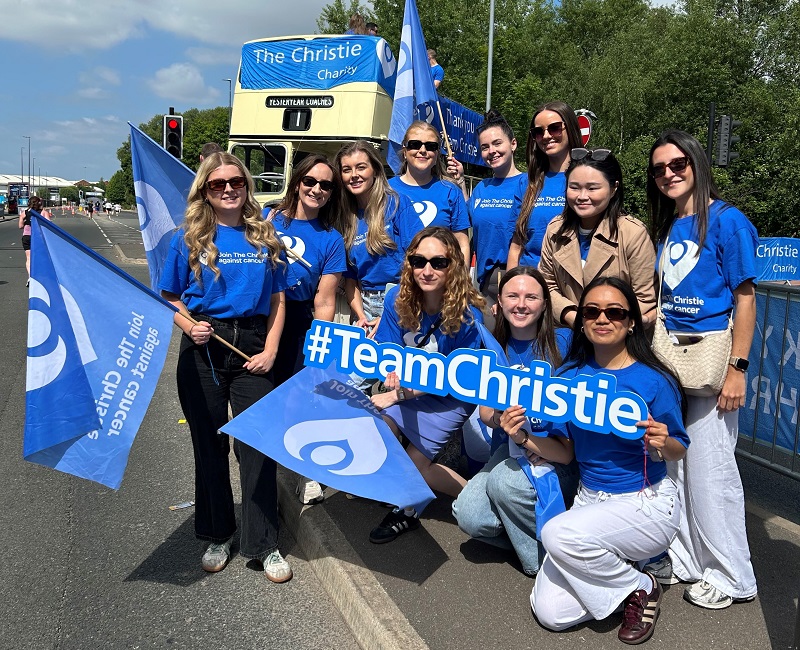 A group of colleagues from Hill Dickinson wearing Christie Charity t-shirts at a sporting event and standing in front of a Christie Charity open-top bus.