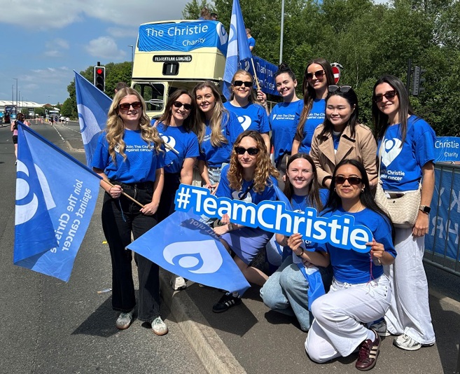 A group of colleagues from Hill Dickinson wearing Christie Charity t-shirts at a sporting event and standing in front of a Christie Charity open-top bus.