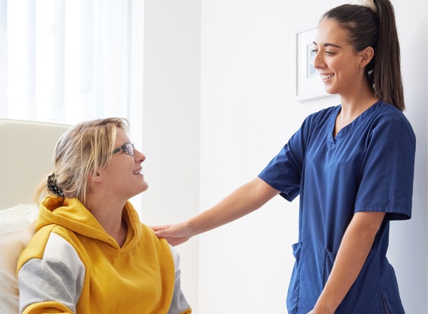 A photo of a nurse looking at a young female patient in a chair.
