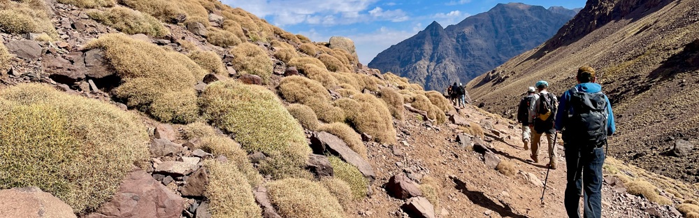 A photo of a trek in Morocco with hikers in the foreground and mountains in the background.