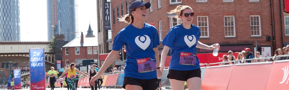 A photo of 2 women in Christie Charity t-shirts running hand-in-hand.