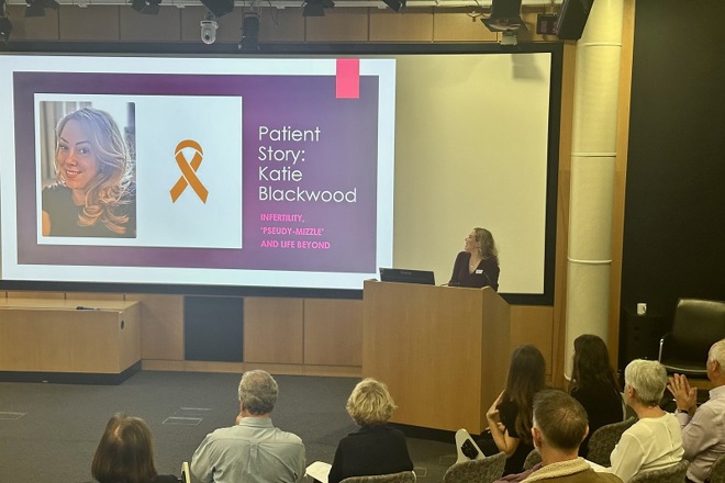 A photo of Christie patient Katie Blackwood presenting at The Christie with a slide that reads 'Patient story: Katie Blackwood. Infertility, 'pseudy-mizzle' and life beyond'.