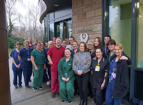 A photo of Christie at Macclesfield staff celebrating the centre's third anniversary, standing outside the centre's entrance.
