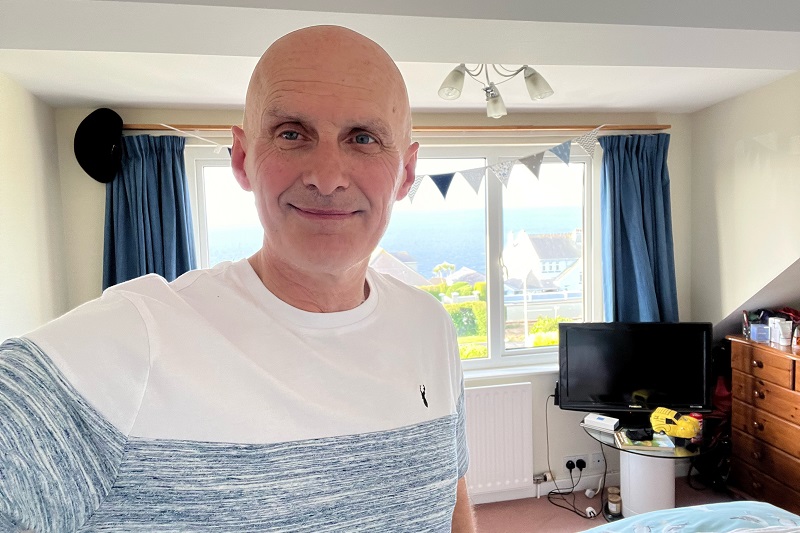 A photo of Christie prostate patient Andy Fleet in a a bedroom with a window and bunting behind him.