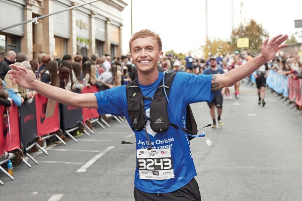 A photo of a man running in a Christie Charity t-shirt with his hands in the air.