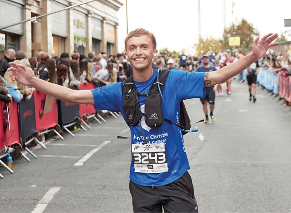A photo of a man running in a Christie Charity t-shirt with his hands in the air.