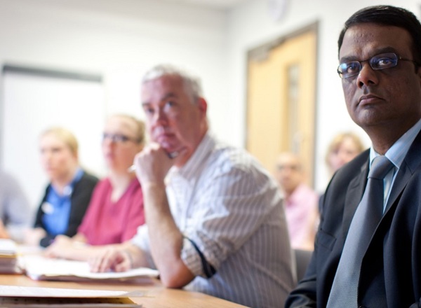 A multi-disciplinary team looking towards the camera, with an Asian doctor in the foreground and some blurred white colleagues in the background.