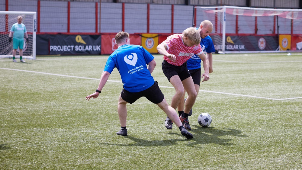 A photo of 3 people playing football, 2 people wearing Christie Charity t-shirts.