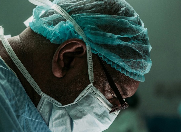 A close-up photo of a man's face in a surgical face mask and hairnet.