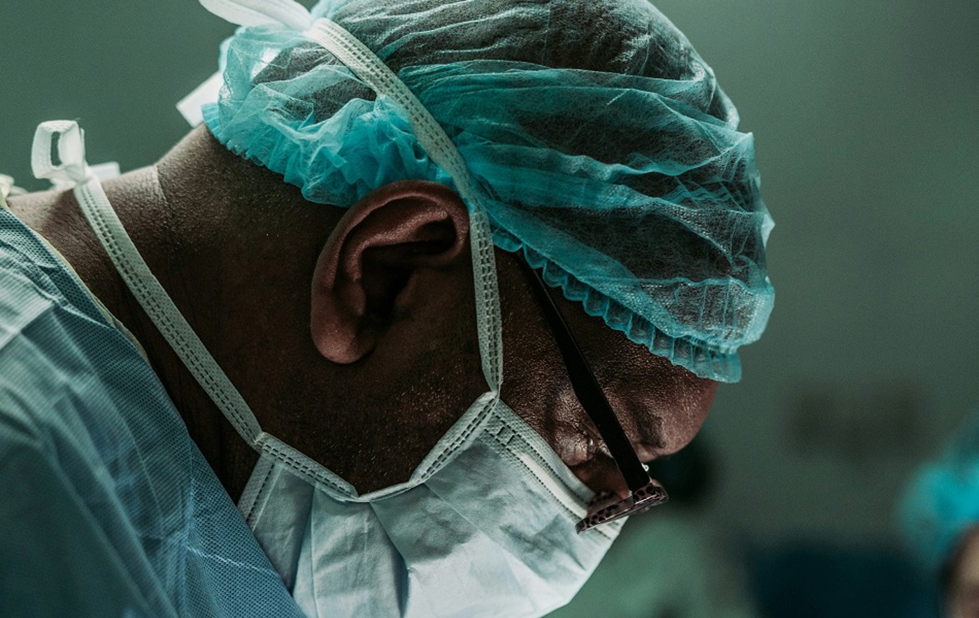 A close-up photo of a man's face in a surgical face mask and hairnet.