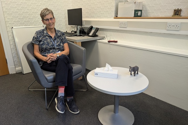 A photo of Anne Crook, recently-retired counsellor at The Christie, sitting next to a coffee table.
