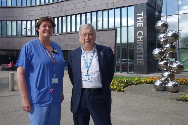 A photo of Christie patient and governor Phil Ormesher on the right, reunited with his consultant radiographer at The Christie Cathy Taylor on the left after 11 years. The 2 are standing in front of the sculpture outside of The Christie entrance.