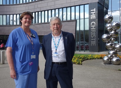A photo of Christie patient and governor Phil Ormesher on the right, reunited with his consultant radiographer at The Christie Cathy Taylor on the left after 11 years. The 2 are standing in front of the sculpture outside of The Christie entrance.