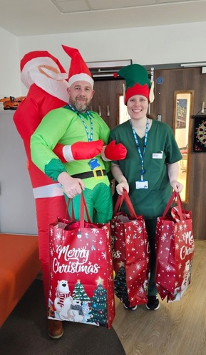 A photo of Steve Harcourt from the teenage and young adult (TYA) service at The Christie dressed as an elf with another colleague and carrying bags of Christmas presents.