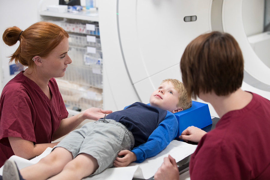 A photo of a child patient being treated with radiotherapy by 2 radiographers.