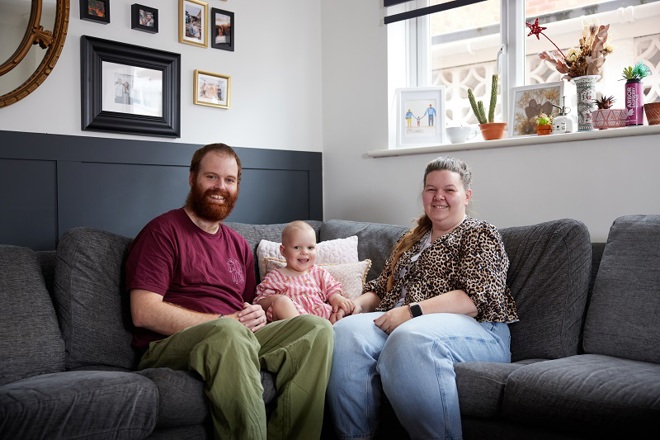 A photo of Richard and Lucy Cook sitting on a couch with their 2-year-old daughter Pippa.