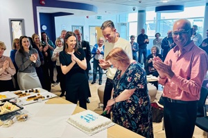 A photo of the Colorectal and Peritoneal Oncology Centre's peritoneal tumour service patient day in 2024. A large group of people are clapping and watching Professor Sarah O'Dwyer cut a cake.