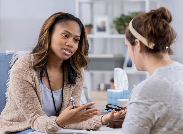 A photo of a young woman speaking compassionately to another young woman in an office.