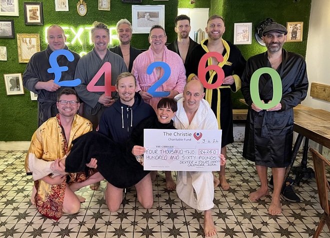 A photo of a group of Christie Charity fundraisers from Knutsford bar Dexter and Jones. 7 men are standing at the back in dressing robes holding numbers which read £4260. 3 men are kneeling at the front, also wearing dressing robes and holding a woman. The woman is holding a cheque reading "The Christie, Four Thousand Two Hundred and Sixty Pounds. Dexter and Jones Charity Calendar 2024".