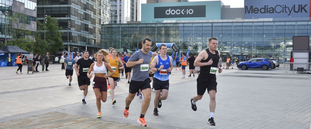 A group of runners running past the Dock 10 building at Media City in Salford.