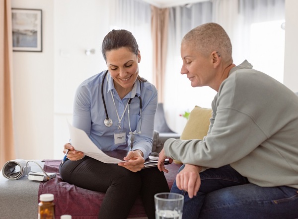 A photo of a female clinician explaining something from a piece of paper to a female patient with a shaved head.
