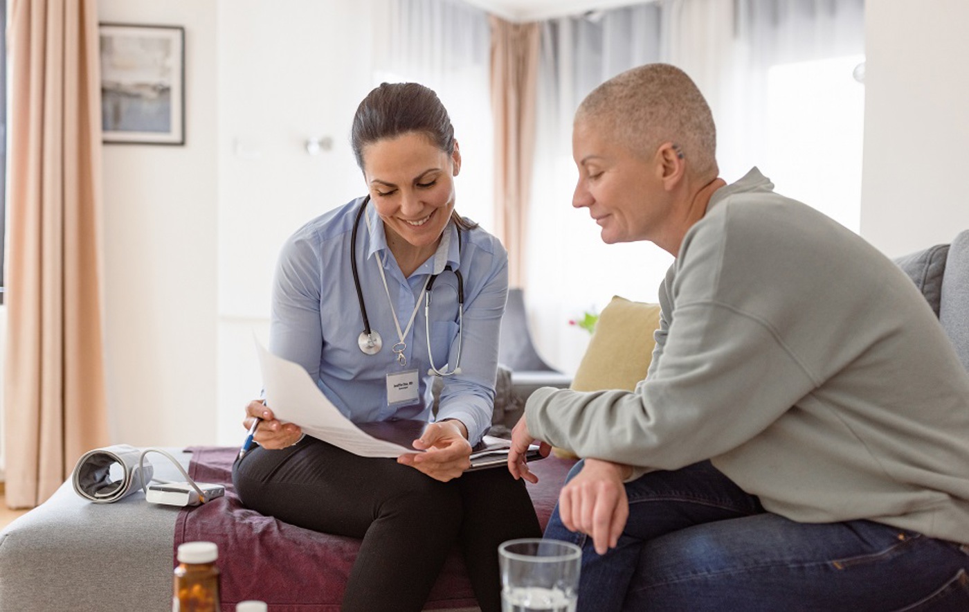 A photo of a female clinician explaining something from a piece of paper to a female patient with a shaved head.