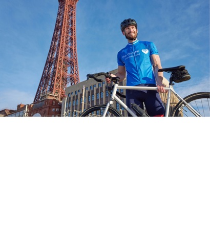 A photo of a male cyclist holding a bike and standing in front of the Blackpool tower.