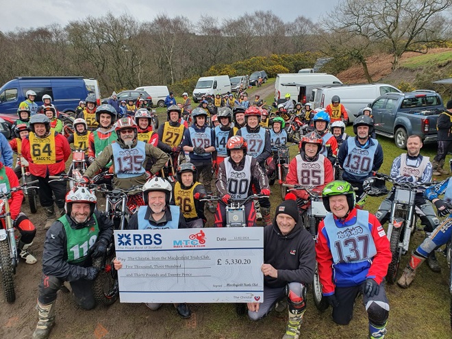 A photo of Macclesfield Trials Club at their fundraising event for The Christie Charity. Around 70 motorcycle riders are pictured, all wearing helmets and seated on their motorcycles. Towards the front of the photo, some of the riders are holding a giant RBS cheque that reads, 'Pay The Christie from the Macclesfield Trials Club, Five Thousand, Three Hundred and Thirty Pounds and Twenty Pence'.