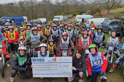 A photo of Macclesfield Trials Club at their fundraising event for The Christie Charity. Around 70 motorcycle riders are pictured, all wearing helmets and seated on their motorcycles. Towards the front of the photo, some of the riders are holding a giant RBS cheque that reads, 'Pay The Christie from the Macclesfield Trials Club, Five Thousand, Three Hundred and Thirty Pounds and Twenty Pence'.