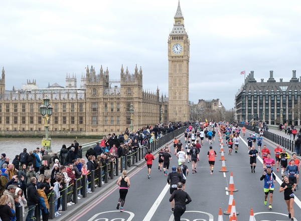 A photo of a running event in front of the Houses of Parliament in London with a group of runners running over the bridge.