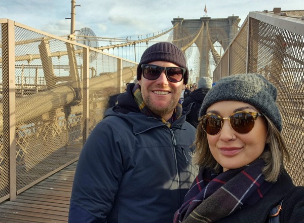 A photo of Paul and Jess Swift both wearing sunglasses and standing on a bridge.