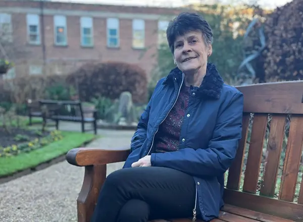 A photo of former Christie patient and supporter Adele Adams sitting on a bench in the garden at The Christie.