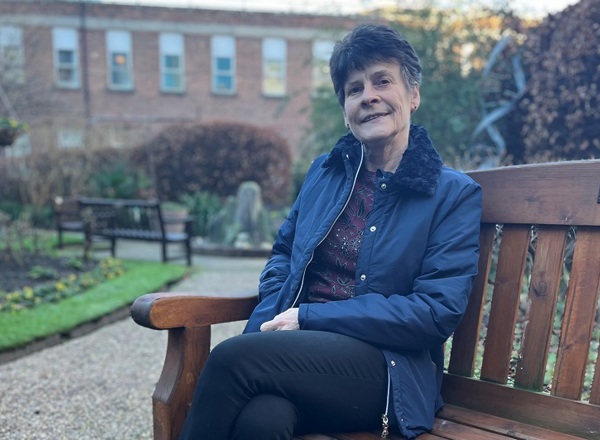 A photo of former Christie patient and supporter Adele Adams sitting on a bench in the garden at The Christie.