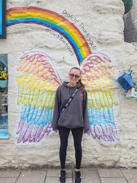 A photo of Christie patient Justine Carson standing in front of rainbow wings.