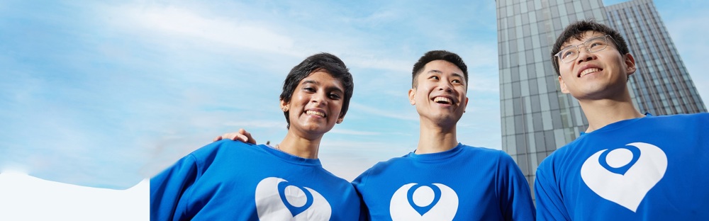 A photo of 3 people wearing Christie Charity t-shirts and standing in front of the Beetham Tower.