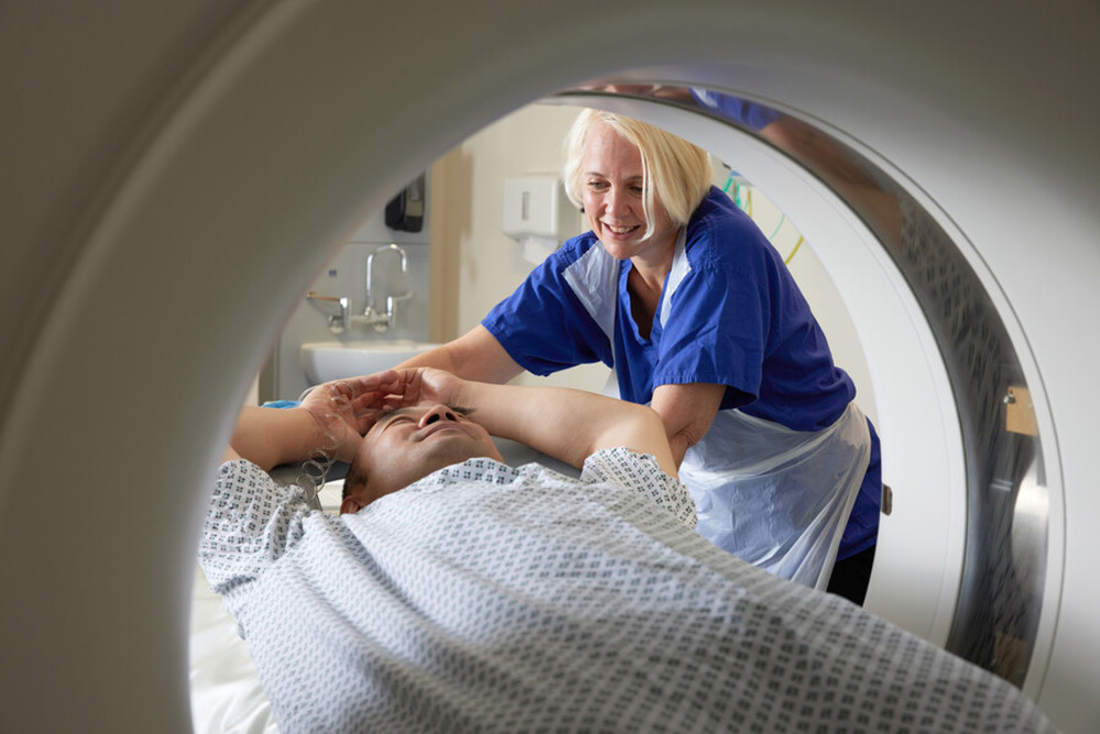 A photo of a man being pushed into a CT scanner by a woman.