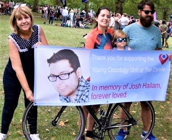 A photo of Christie fundraiser Michelle Foster holding a banner with a woman, a man and a small child. The small child is sitting on a bike, which is behind the banner. The banner reads, "Thank you for supporting the Young Oncology Unit at The Christie. In memory of Josh Hallam, forever loved."