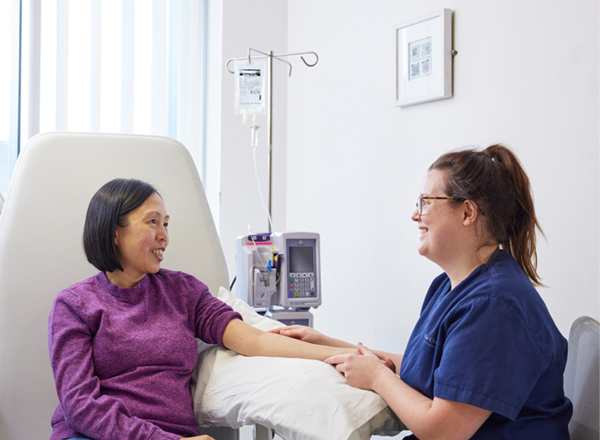 A photo of a woman receiving cancer treatment in a chair from a female staff member.