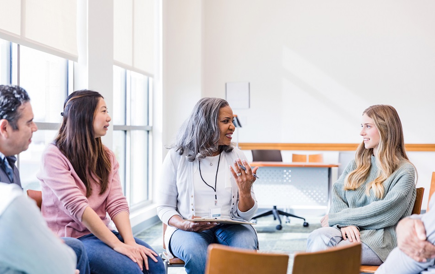 A photo of 3 women and 1 man sitting around in a circle and talking.