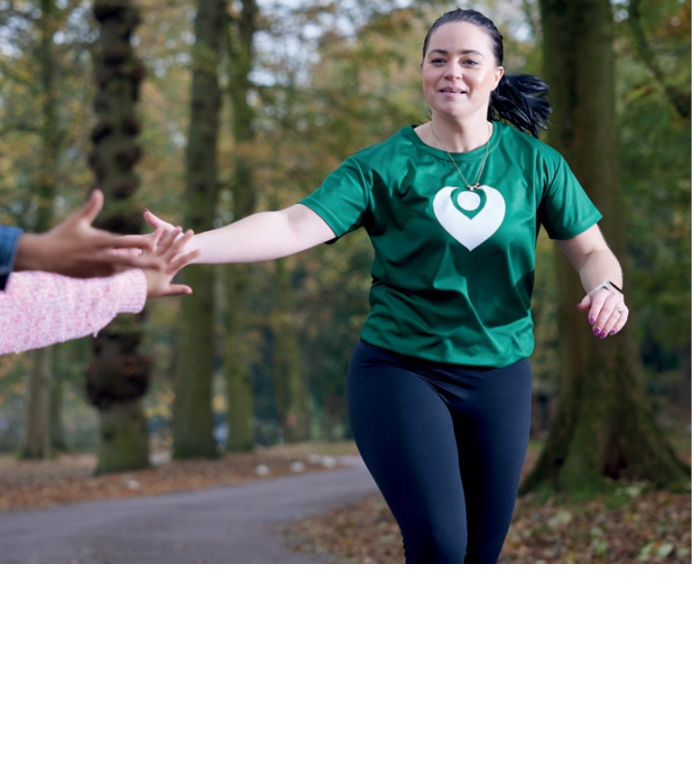 A photo of a woman running through a forest wearing a green Christie Charity t-shirt.