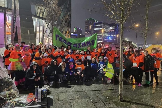 A photo of a group of 57 fundraisers in neon orange Christie Charity t-shirts standing outside The Lowry theatre and gallery complex.