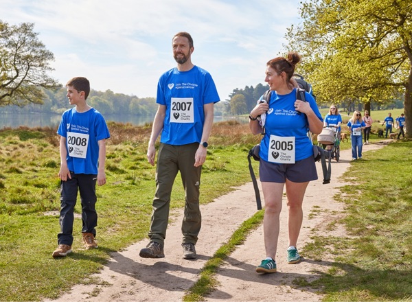 A photo of a group of people in Christie Charity t-shirts and sunglasses walking through a park.