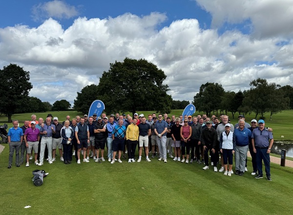 A photo of a large groups of golfers standing at a golf course, with Christie Charity banners in the background.