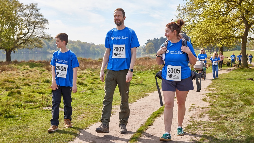A photo of a group of people in Christie Charity t-shirts and sunglasses walking through a park.