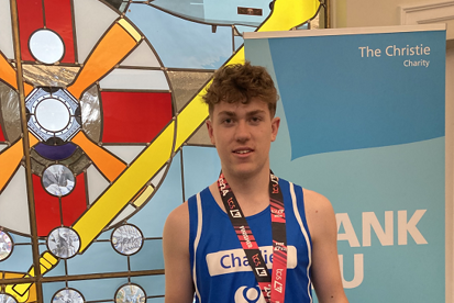 A photo of Christie Charity fundraiser Charlie Balls in a Christie running vest, wearing a London Marathon medal and holding a green 'I did it for The Christie' sign.