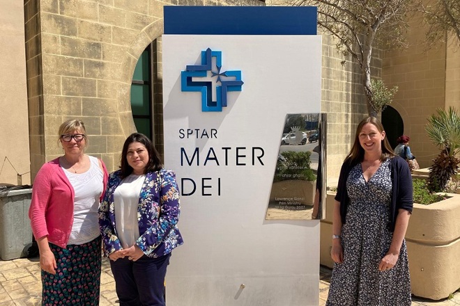 A photo of Julia Handley, Rachael Edwards and Dorothy Aquilina standing next to a MATER DEI Hospital sign in Malta.